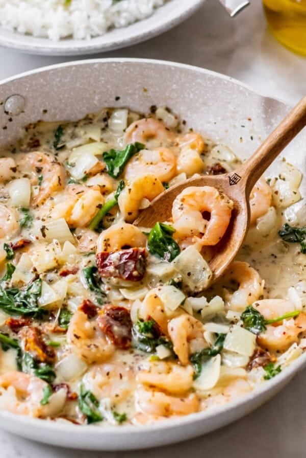 Tuscan shrimp recipe cooked in a skillet with a wooden spoon resting in the dish.