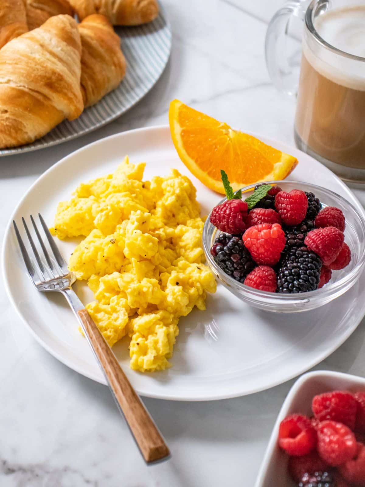 Scrambled eggs with greek yogurt on a plate with a fork to the side. 