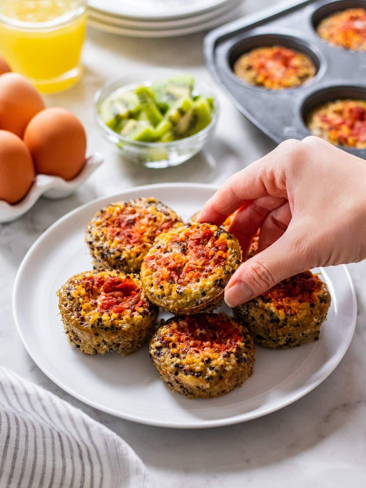 A hand reaching to lift a quinoa egg bite from a pile on a plate.