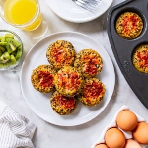 Quinoa egg bites topped with salsa stacked on a plate with more in the muffin tin to the side.