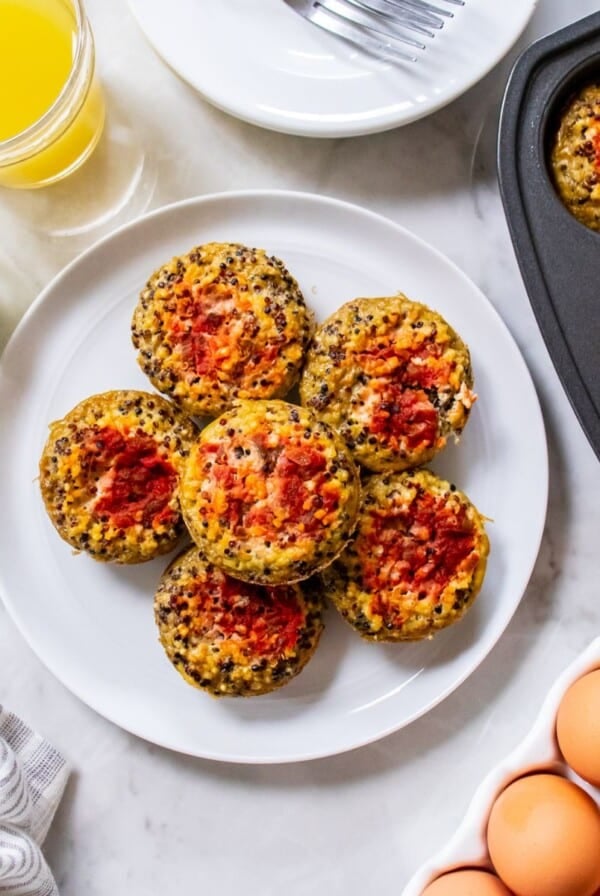 Quinoa egg bites topped with salsa stacked on a plate with more in the muffin tin to the side.