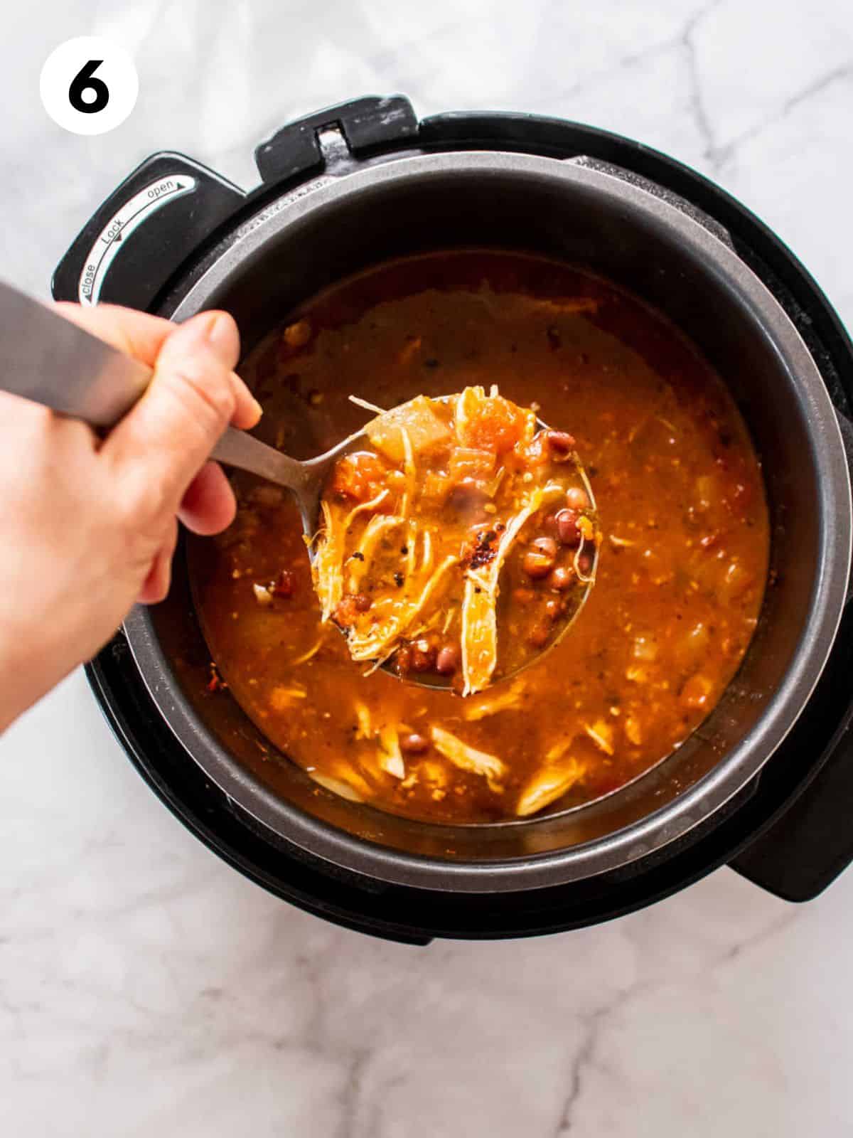 A hand holding a ladle scooping up a serving of chicken taco soup.