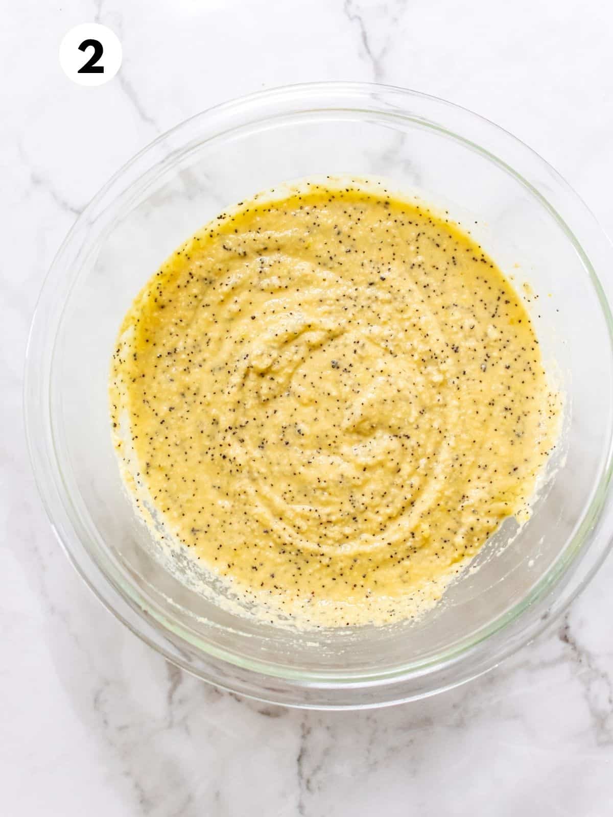 A clear glass bowl containing lemon poppy seed cake mixture.