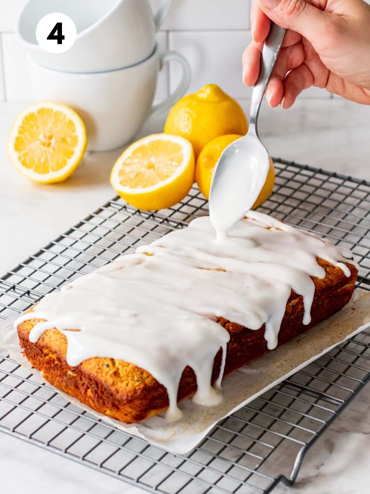 A hand holding a spoon drizzling frosting over a lemon cake.