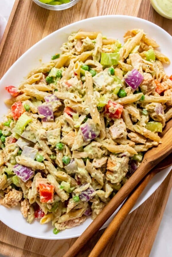 A platter of healthy tuna pasta salad with wooden serving spoons on the side.