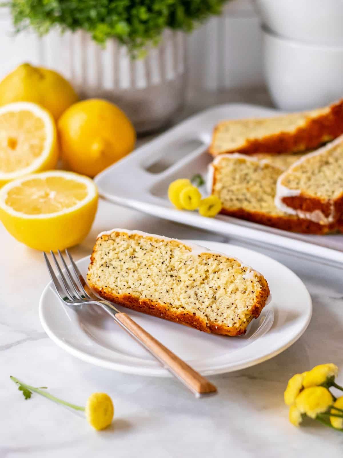A piece of healthy lemon loaf sitting on a white plate with a fork resting to one side.