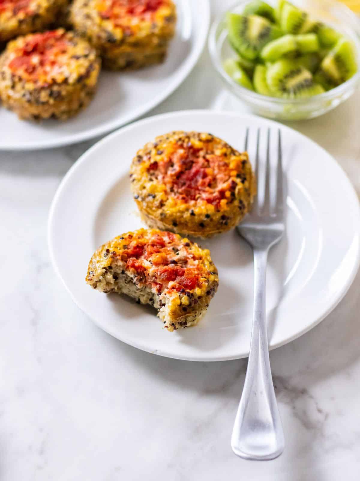 Two quinoa egg bites on a plate with a fork and a bite missing from one. 