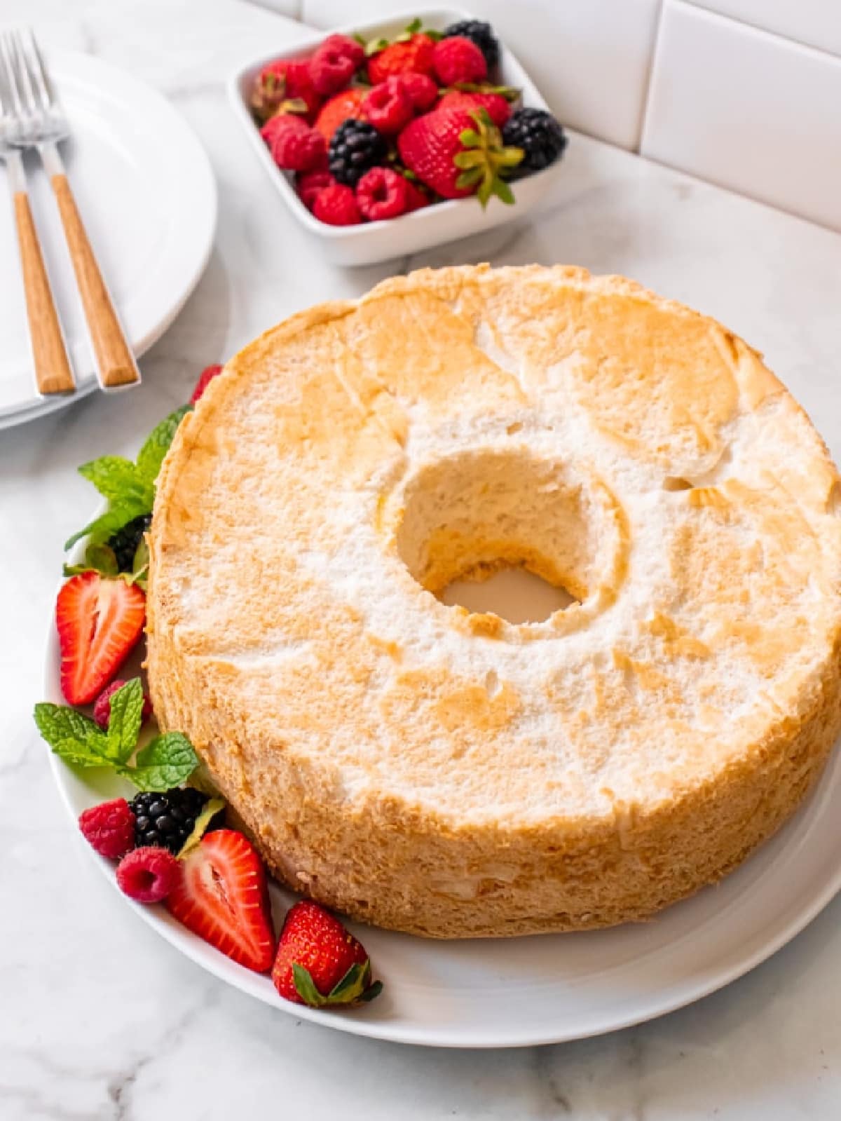 angel food cake on a white plate with sliced strawberries.