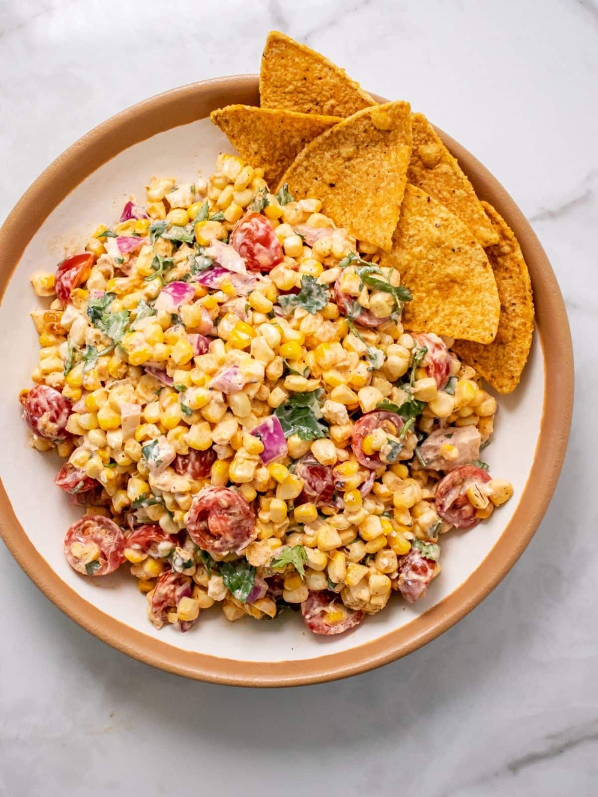 High protein street corn in a brown and cream bowl, with tortilla chips on the side.