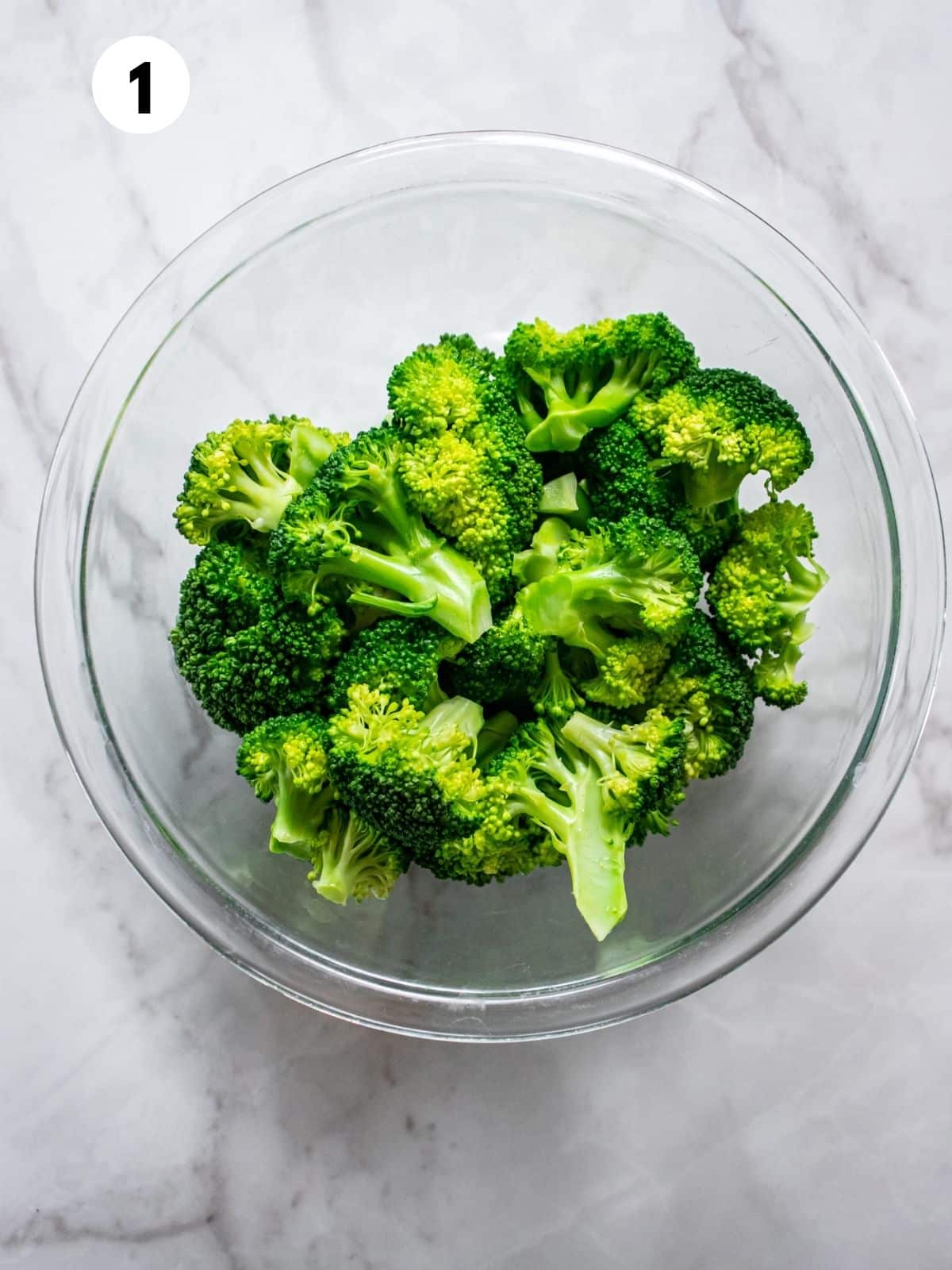 Raw broccoli florets in a glass bowl.