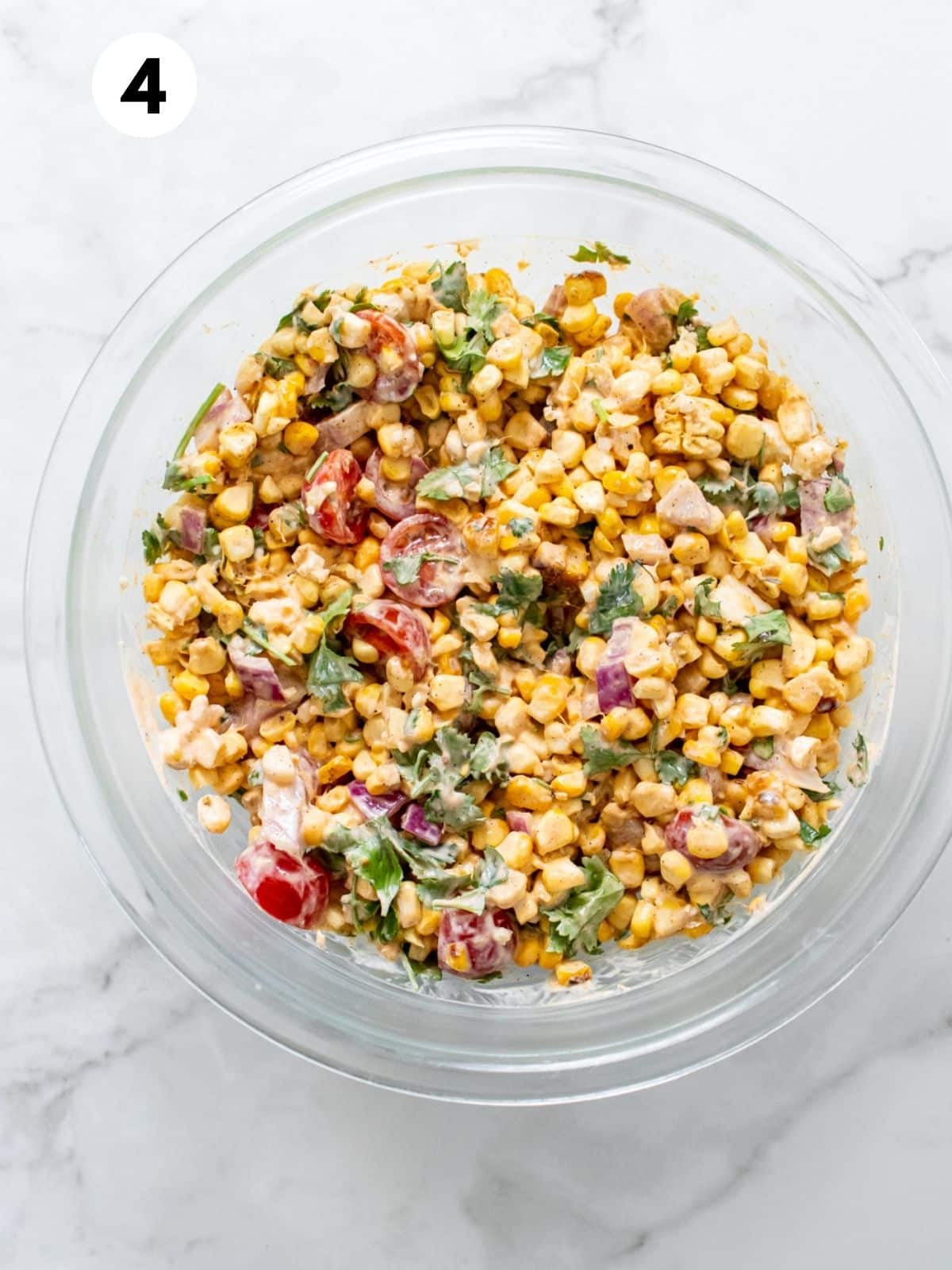 Mexican street corn ready to be served in a glass bowl on a white marbled countertop.