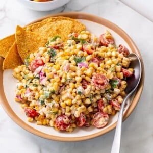 Healthy Mexican street corn salad in a serving bowl, with tortilla chips on one side and a spoon on the other.