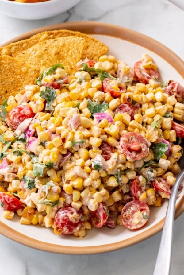 Healthy Mexican street corn salad in a serving bowl, with tortilla chips on one side and a spoon on the other.