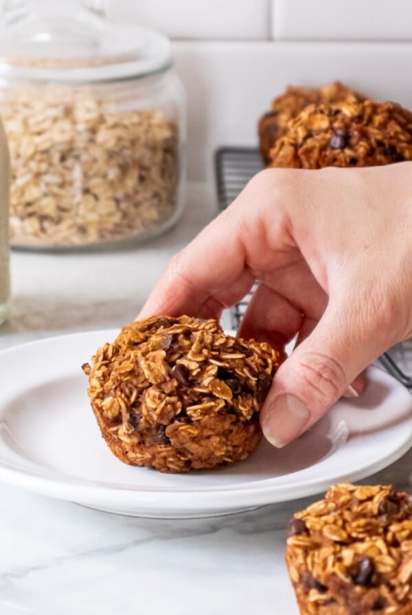 A hand picking up a peanut butter banana muffin off a white plate.