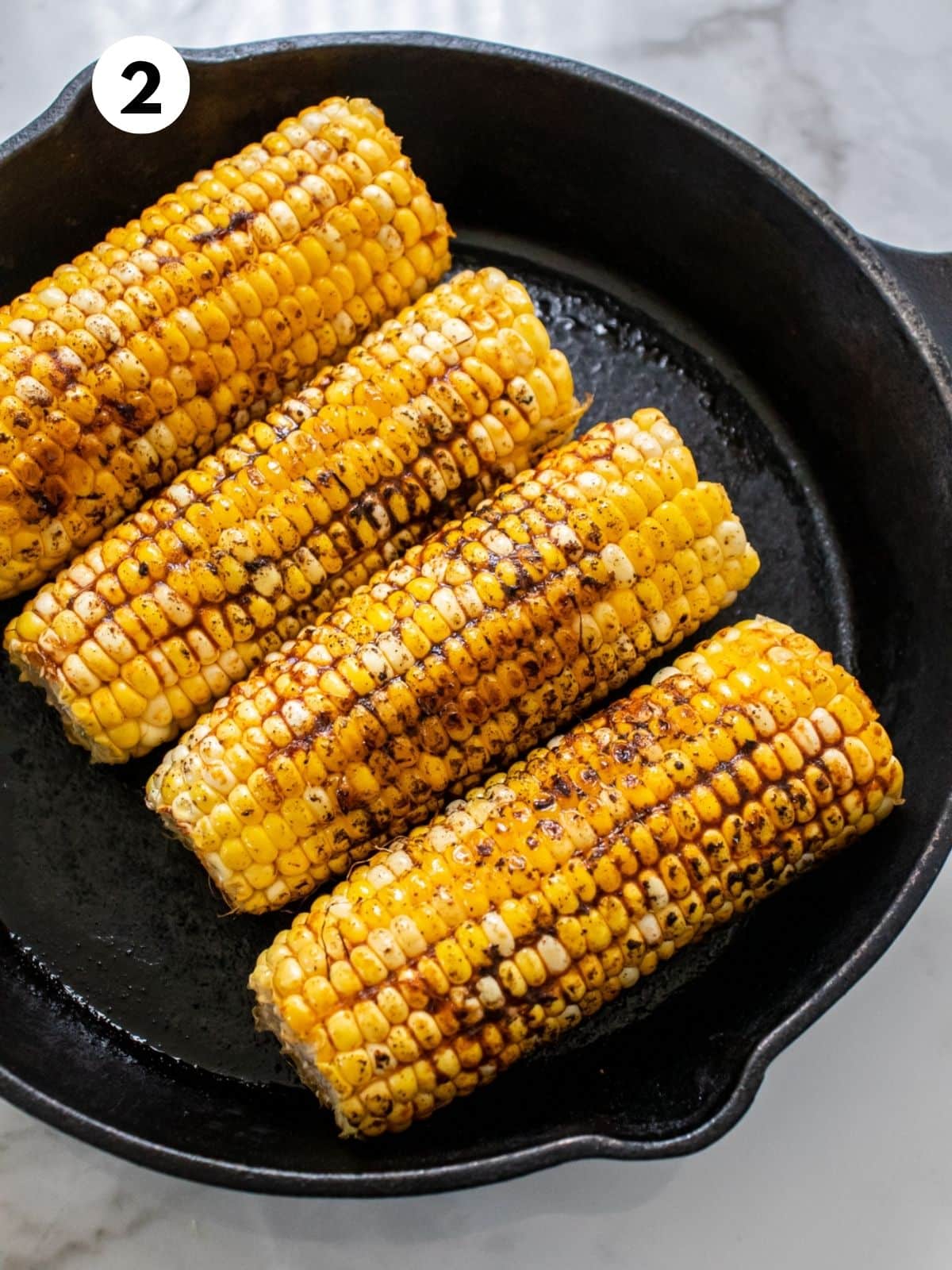 Seasoned, cooked corn cobs sitting in a black skillet.