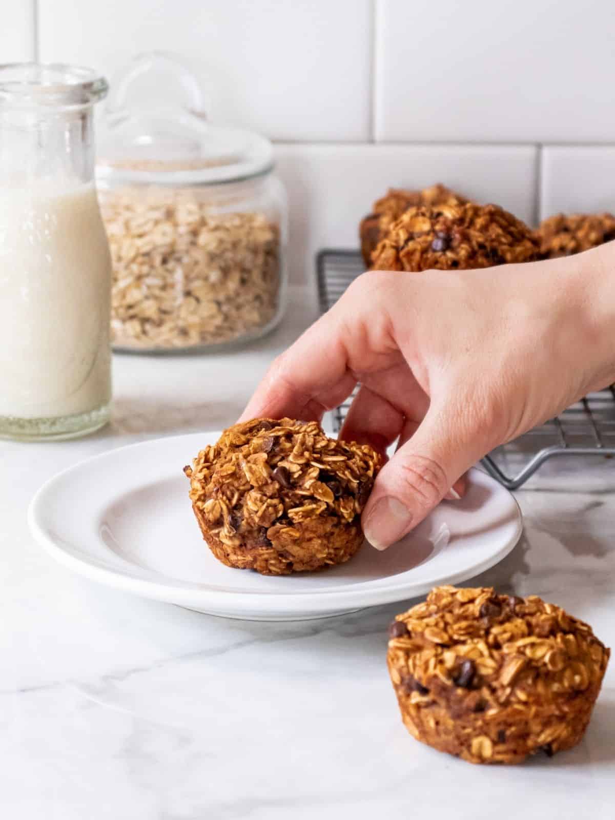 A hand picking up a peanut butter banana muffin off a white plate. 