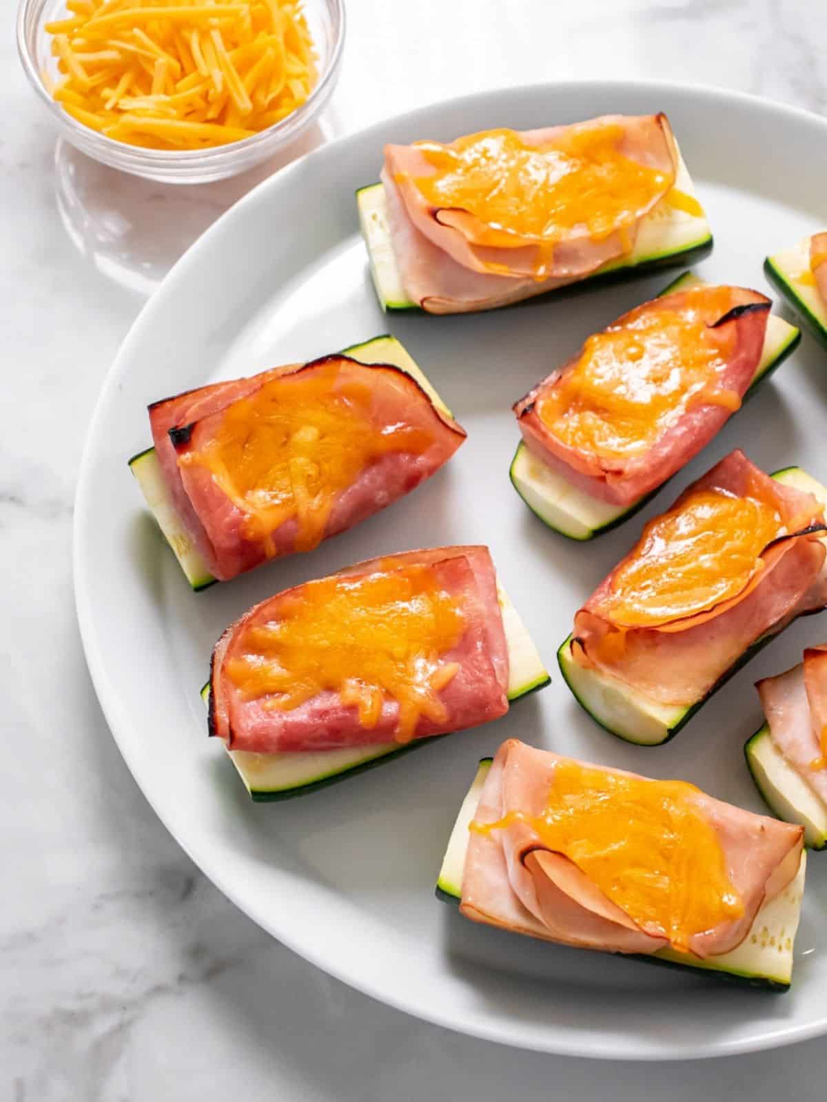 Ham and turkey healthy zucchini boats with melted cheese presented on a white plate.