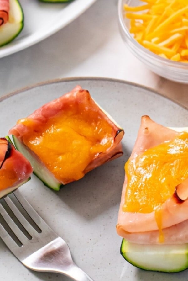 Healthy zucchini boats with lunch meat and cheese on a plate with a fork holding a bite.