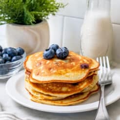 four pancakes stacked on a white plate with a fork.