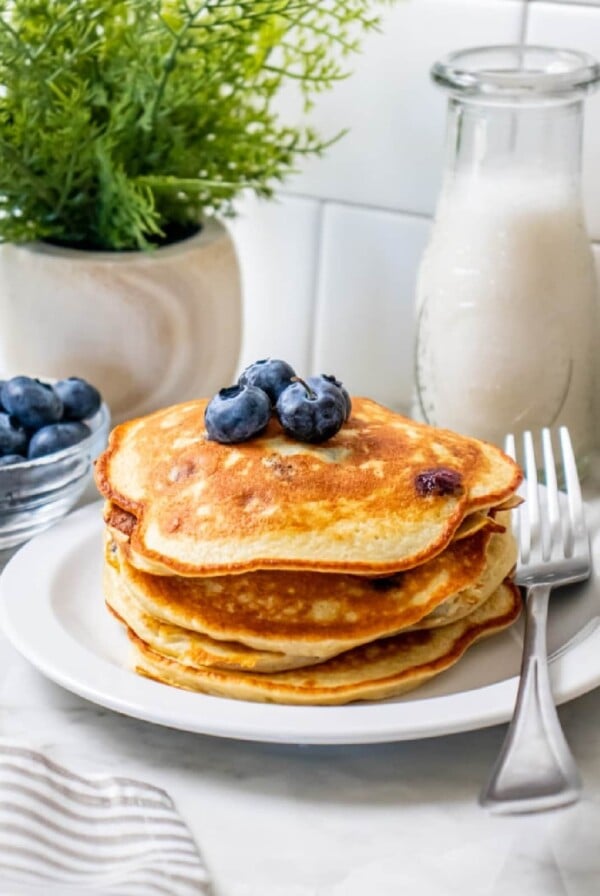 four pancakes stacked on a white plate with a fork.