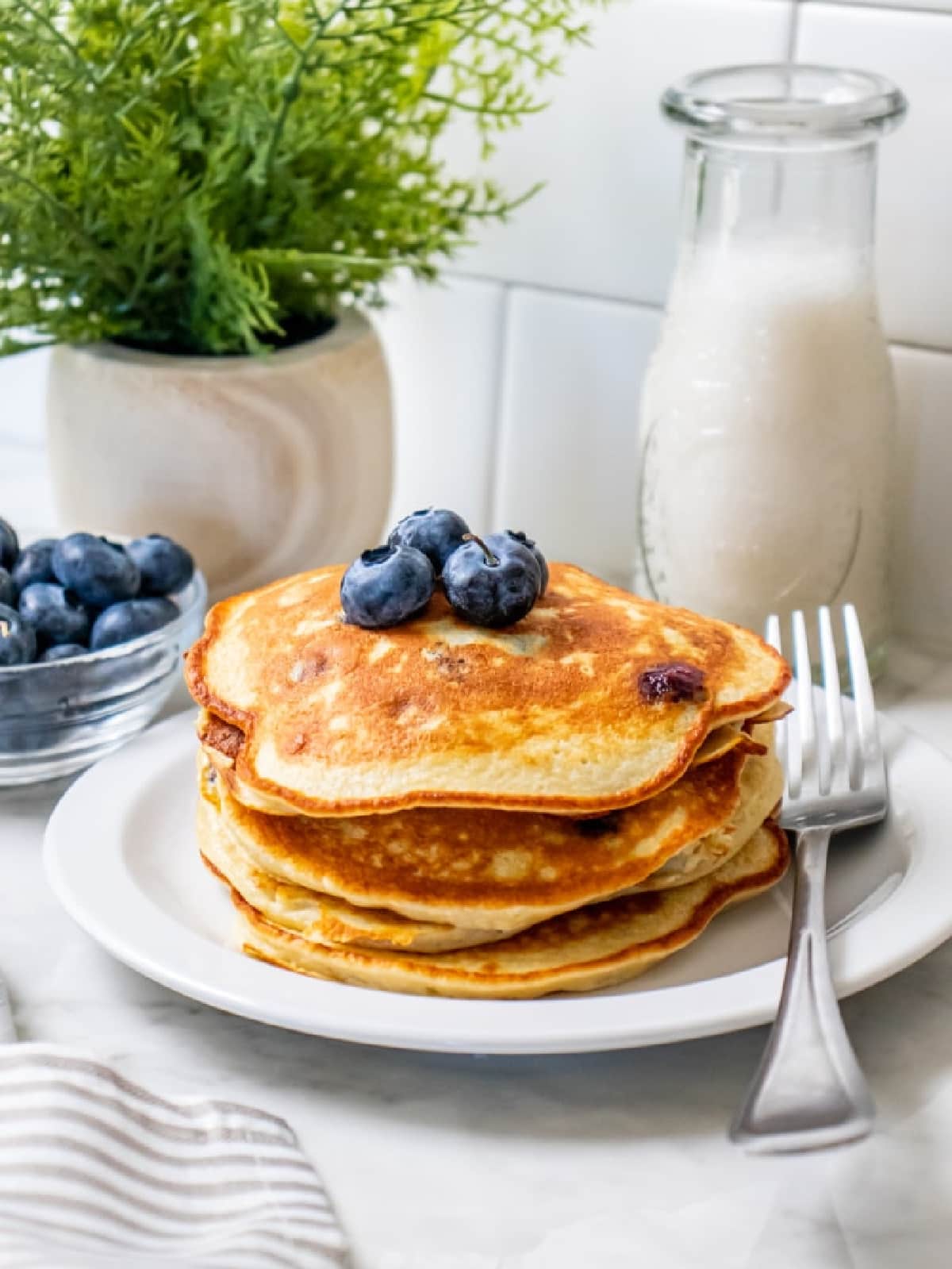 four pancakes stacked on a white plate with a fork.