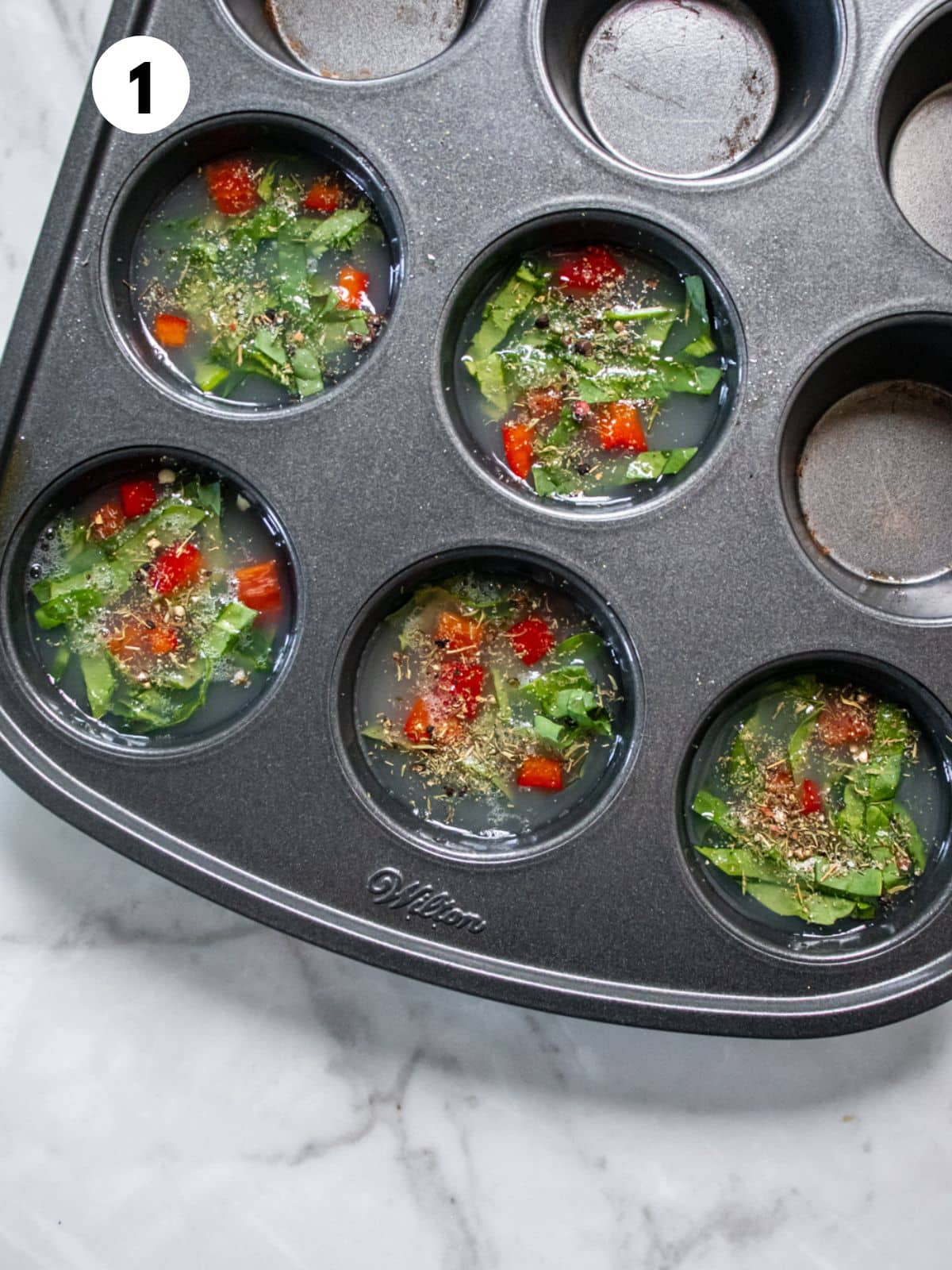 Egg whites, veggies, and seasonings added to a mini muffin pan.