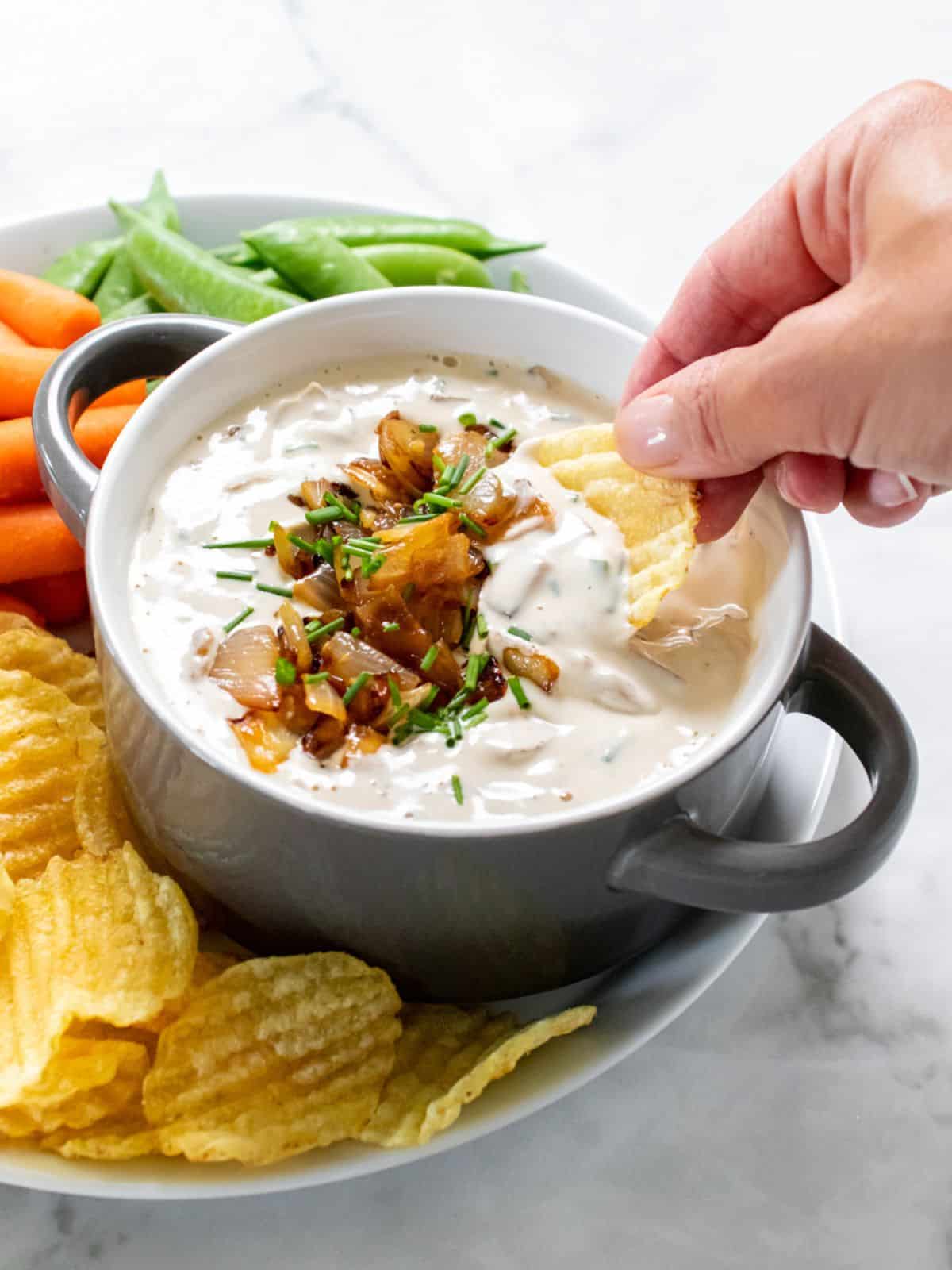 A hand dipping a chip into healthy French onion dip.