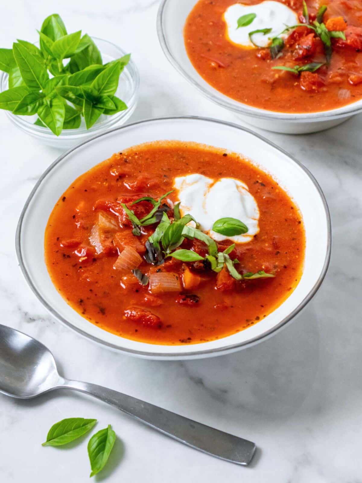 A healthy and simple homemade tomato soup recipe in white bowls on a table.