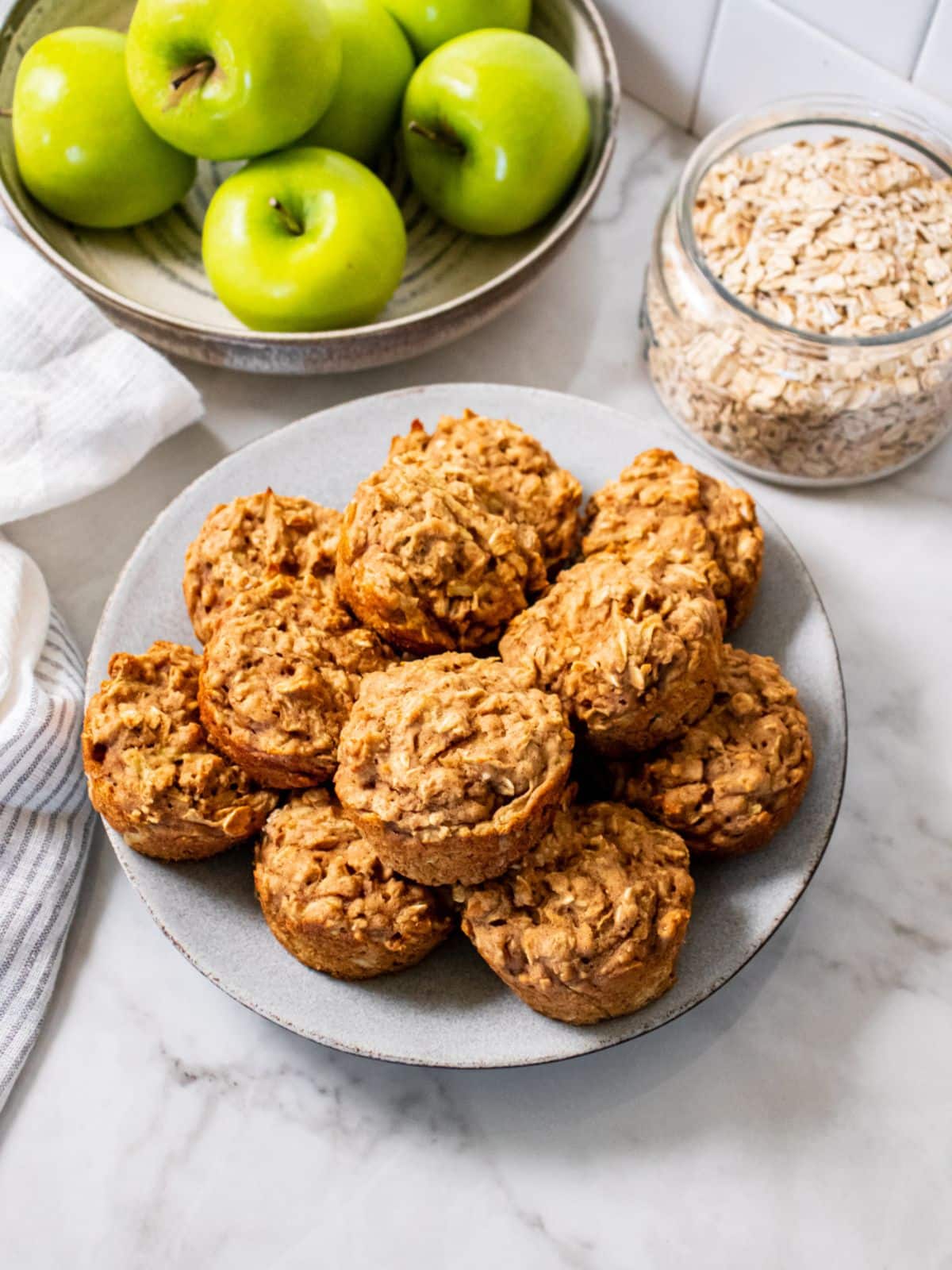 A plate of Greek yogurt apple muffins on the table next to a bowl of apples.
