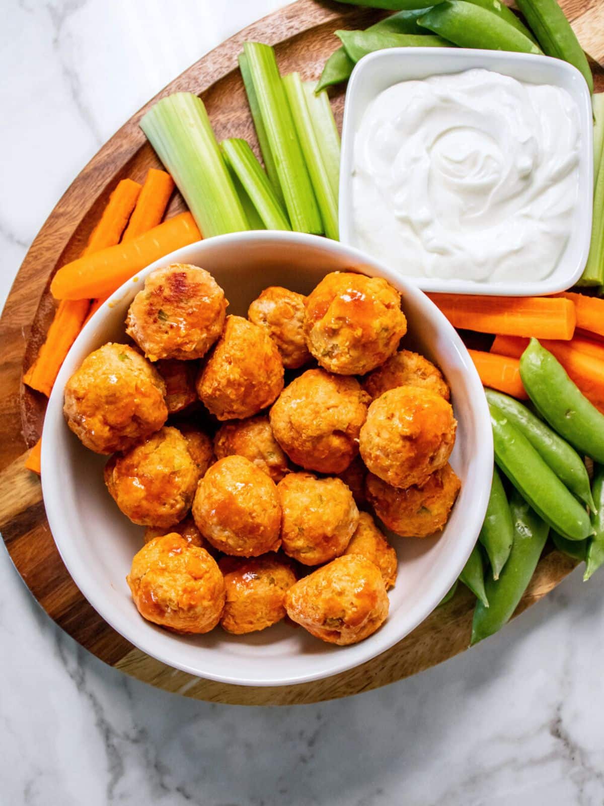 A bowl of healthy buffalo chicken meatballs on a platter with celery, carrots, and a white dip.