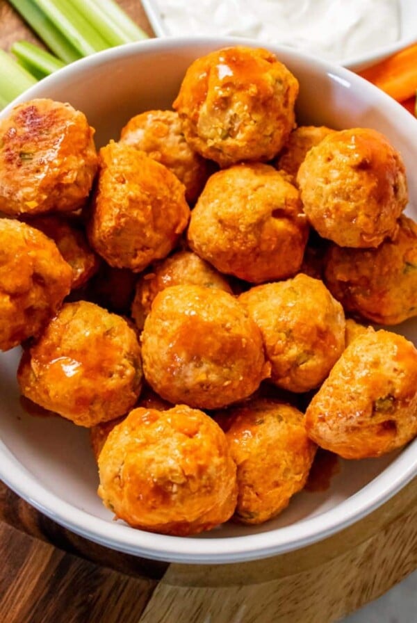 Healthy buffalo chicken meatballs in a white bowl on a round wooden cutting board.