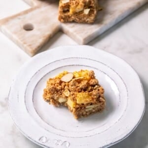 An apple crumble bar sitting on a white plate on a kitchen countertop.