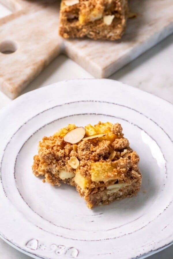 An apple crumble bar sitting on a white plate on a kitchen countertop.