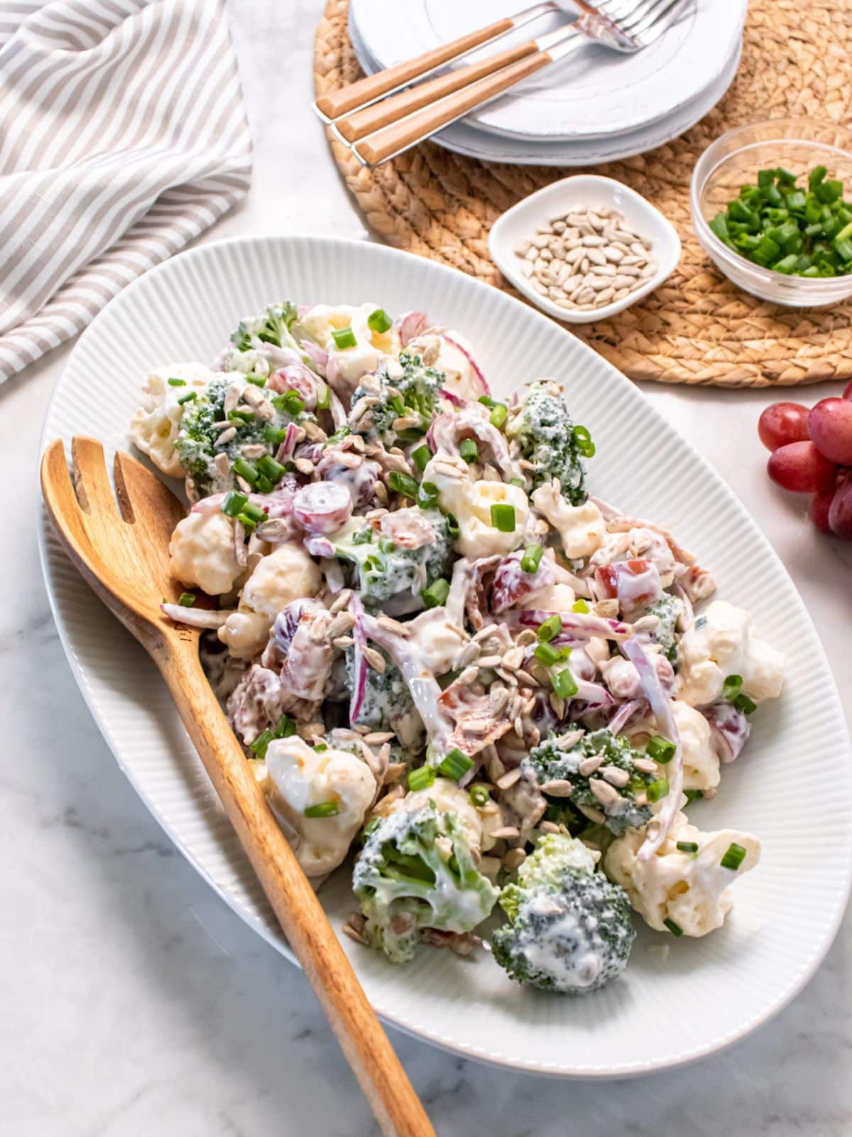 A platter of healthy broccoli and cauliflower salad with a wooden spoon resting to the side.