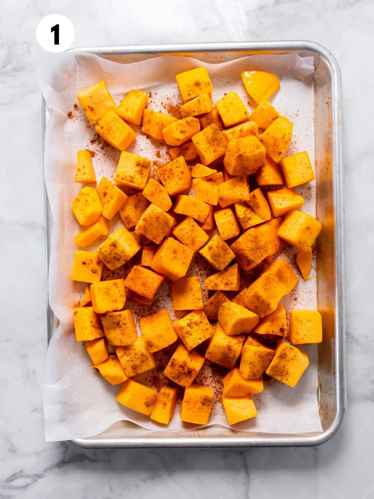 Cubes of butternut squash on a parchment-lined baking tray.