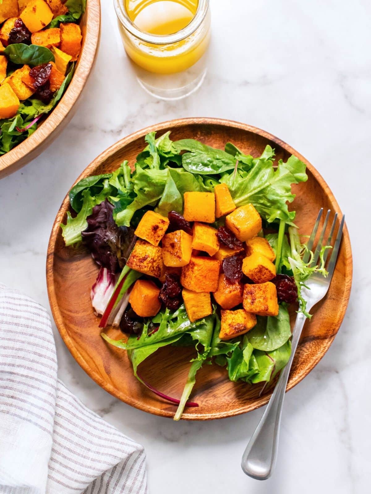 Butternut squash salad served on a wooden plate with a fork resting to one side.