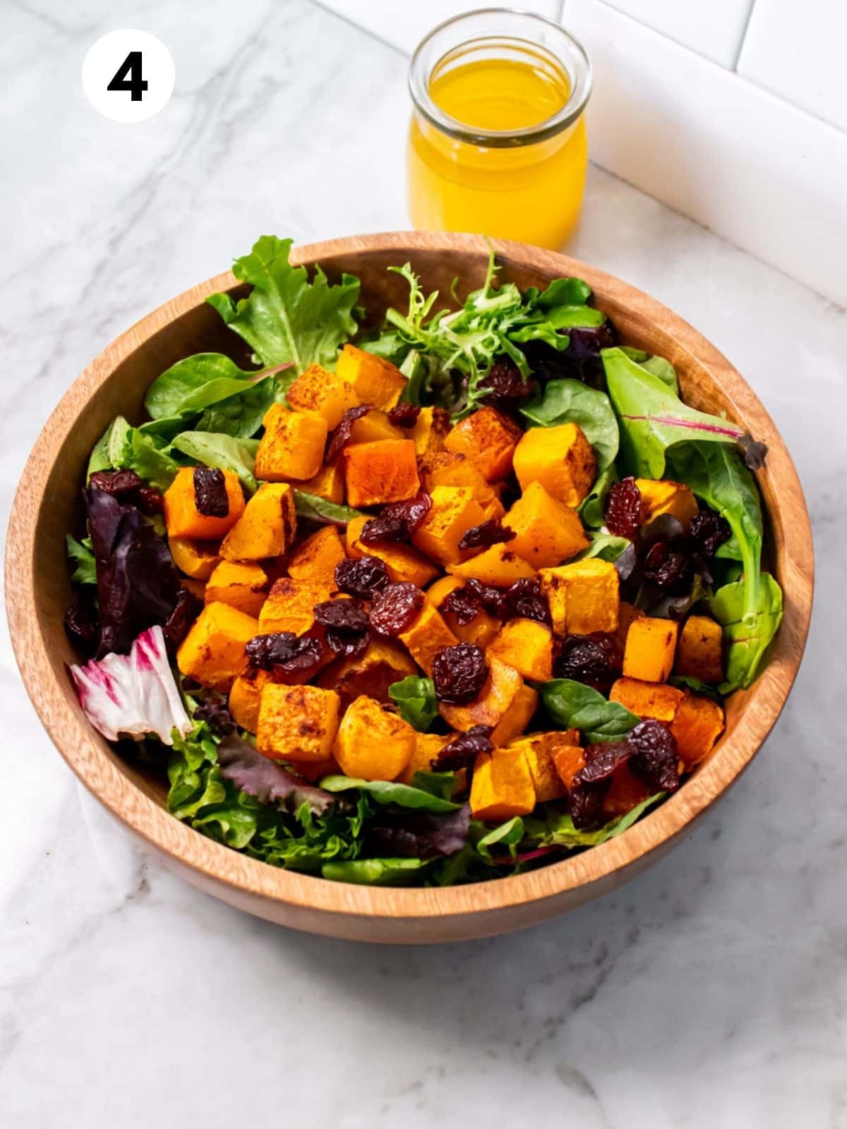 A wooden bowl of butternut cranberry salad with a glass jar of dressing behind.