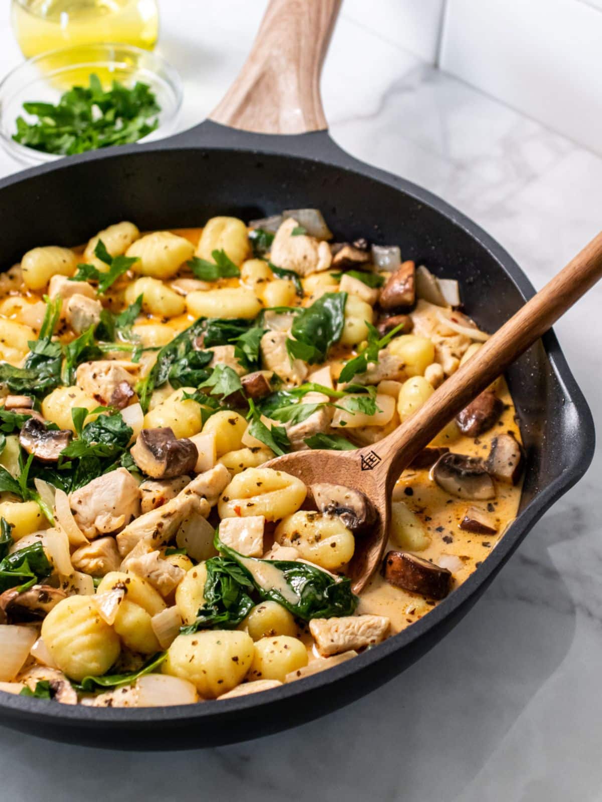  A skillet of chicken and gnocchi with a wooden spoon scooping up a bit.