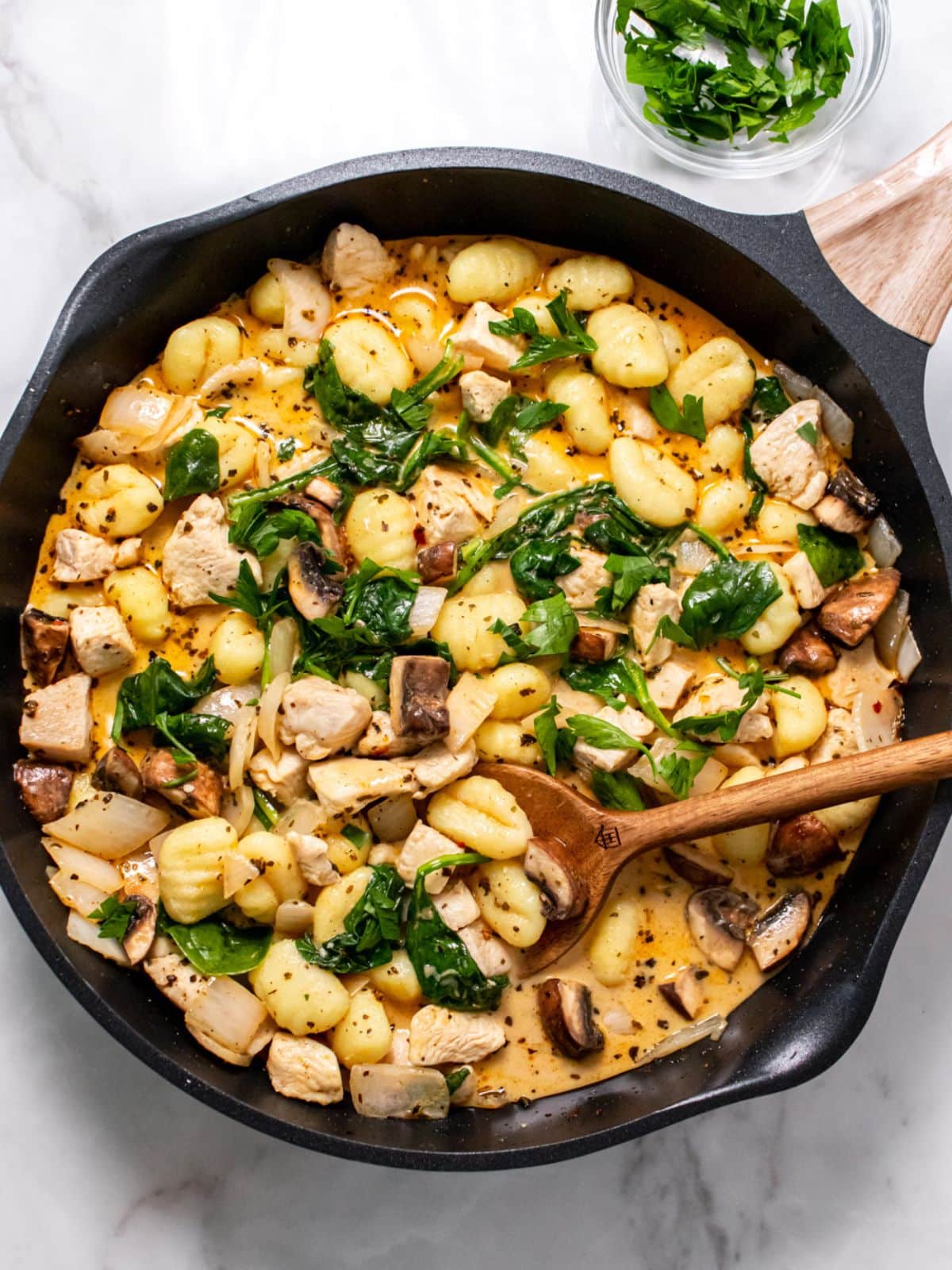 A skillet of chicken and gnocchi with a wooden spoon resting in the skillet.