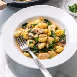A plate of chicken and gnocchi on a table with a fork resting in the dish.