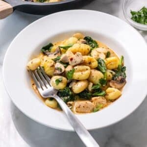 A plate of chicken and gnocchi on a table with a fork resting in the dish.