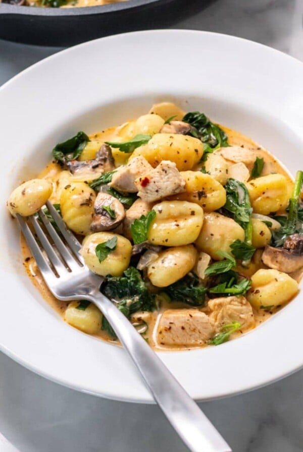 A plate of chicken and gnocchi on a table with a fork resting in the dish.