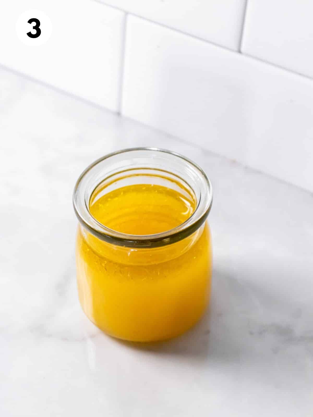 A glass jar of yellow citrus dressing on a white countertop.