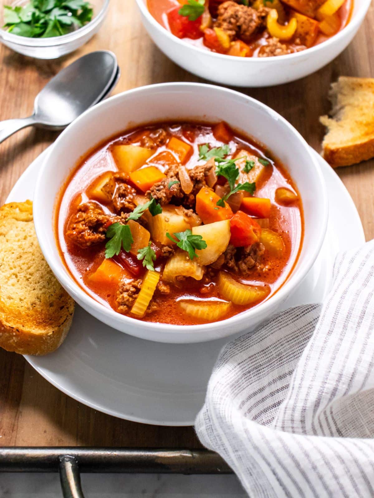 Two bowls of healthy old-fashioned beef vegetable soup on the table with spoons and bread.