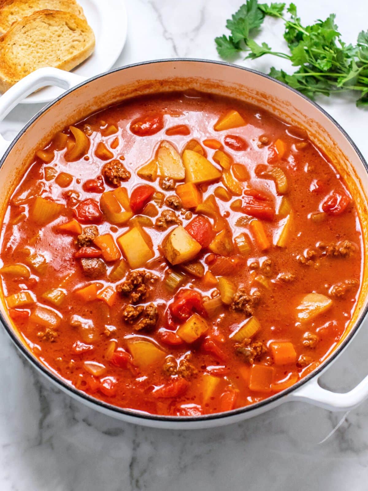 Healthy Beef Vegetable Soup in a large pot on a table with sprigs of parsley and slices of toast on a plate.