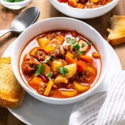 A bowl of healthy old-fashioned beef vegetable soup with a piece of toast to the side.