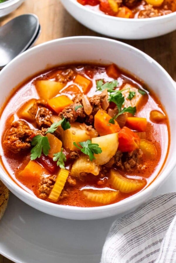 A bowl of healthy old-fashioned beef vegetable soup with a piece of toast to the side.