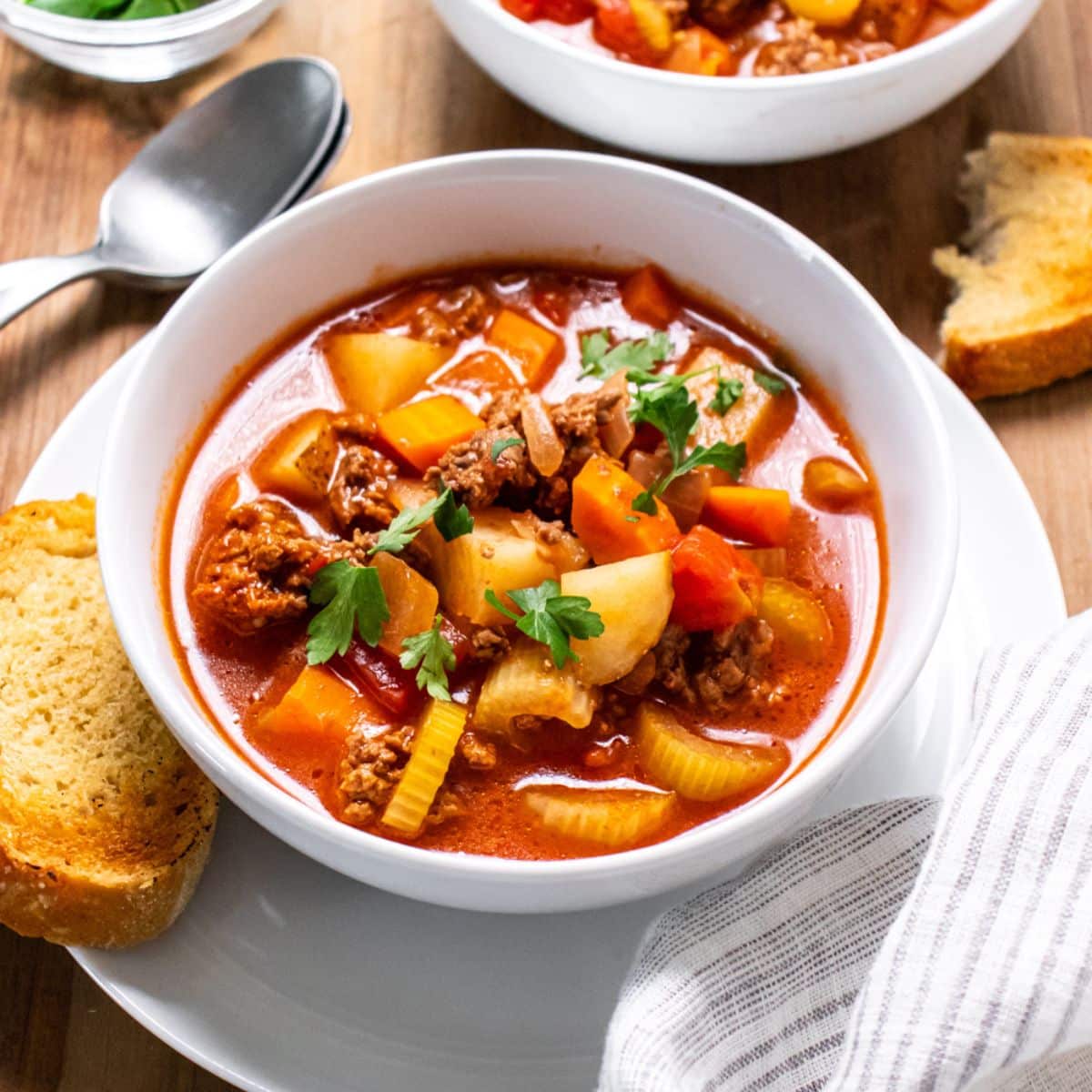 A bowl of healthy old-fashioned beef vegetable soup with a piece of toast to the side.