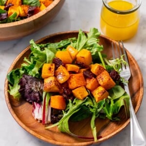 Roasted butternut squash salad served on a wooden plate with a fork on the side of the plate.