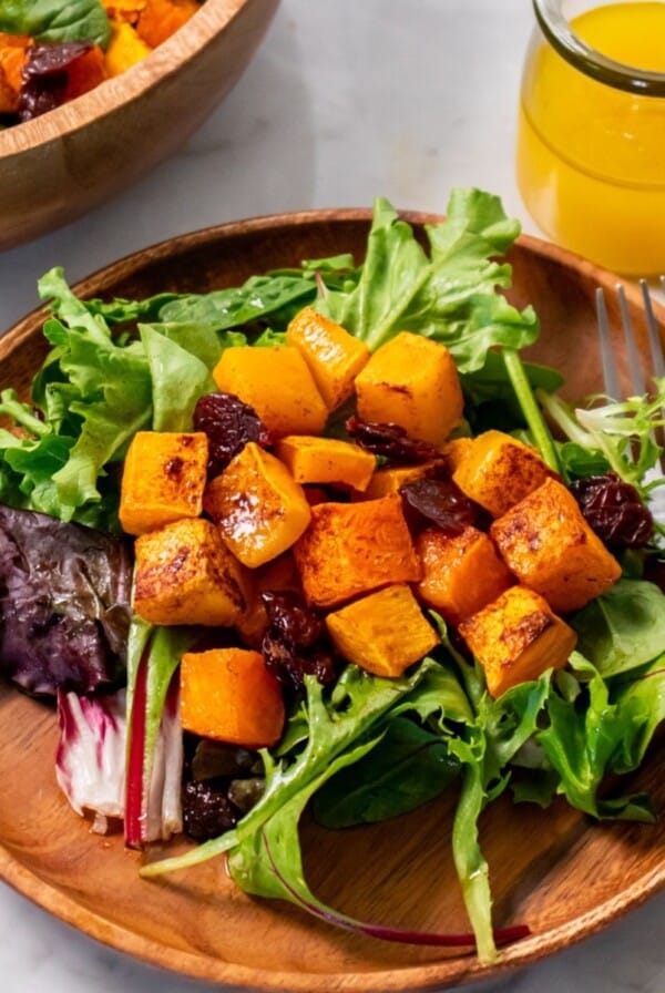 Roasted butternut squash salad served on a wooden plate with a fork on the side of the plate.
